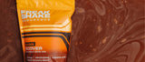 Freak Shake Chocolate Post Workout Recovery Shake in orange packaging floating in chocolate shake